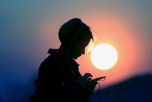 Silhouette d'une fille avec un téléphone portable sur fond de coucher de soleil