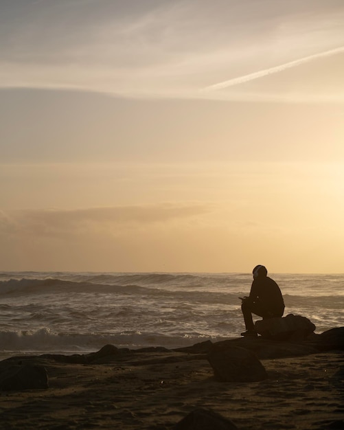 Silhouette d'un garçon assis avec un casque sur la plage du bord de mer au coucher du soleil