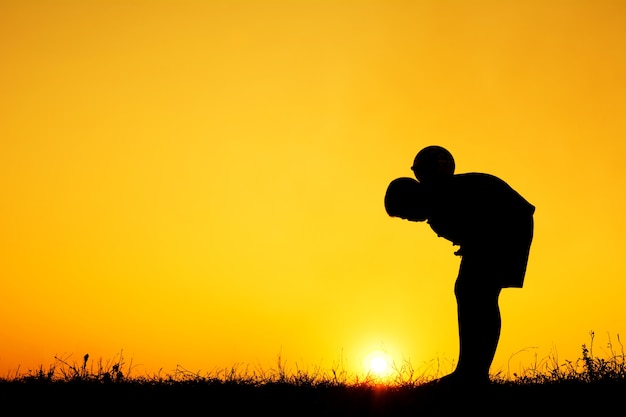 Silhouette de garçon jouant au football pendant le fond de ciel coucher de soleil