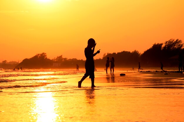 Silhouette de garçon marchant sur la plage au coucher du soleil