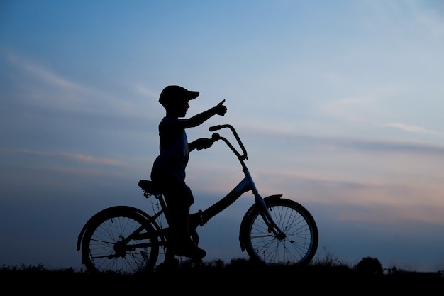 Une silhouette d'un garçon sur un vélo dans la nature