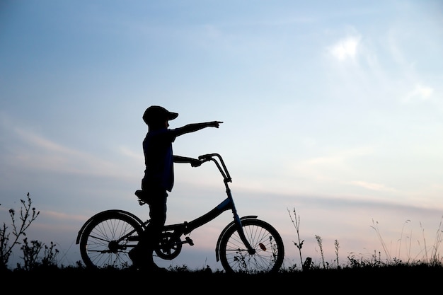 Une silhouette d'un garçon sur un vélo dans la nature