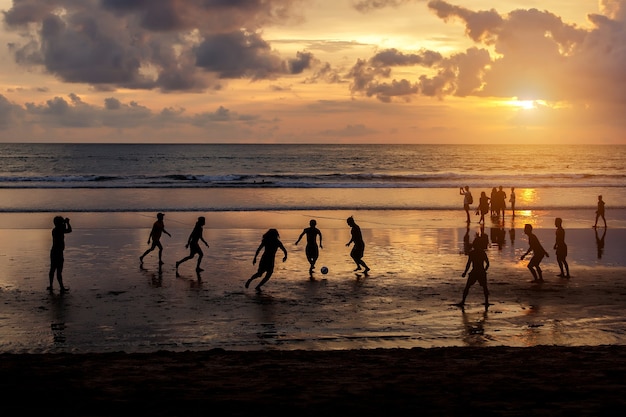 Silhouette d'habitants jouant au football au coucher du soleil.