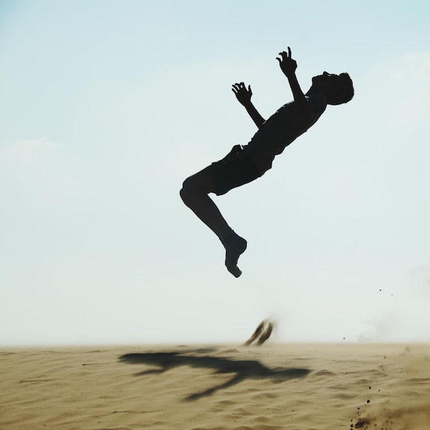 Photo silhouette d'un homme adulte sautant sur le sable à la plage contre un ciel clair