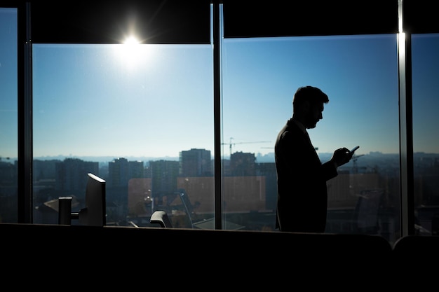 Silhouette d'homme d'affaires dans un bureau moderne sur fond de fenêtre, l'homme utilise le téléphone