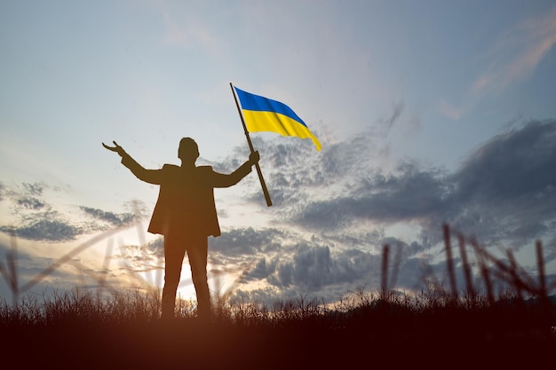 Silhouette d'un homme d'affaires tenant le drapeau ukrainien avec fond de lever de soleil