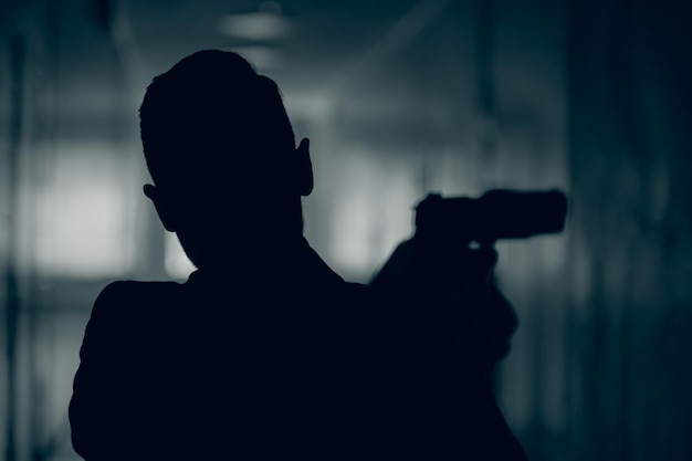 Silhouette d'un homme avec une arme dans un couloir sombre en gros plan