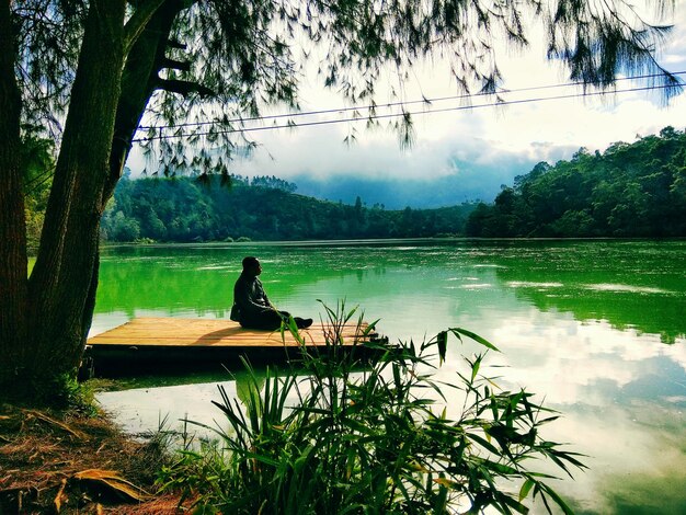 Silhouette d'un homme assis au bord d'un lac contre le ciel