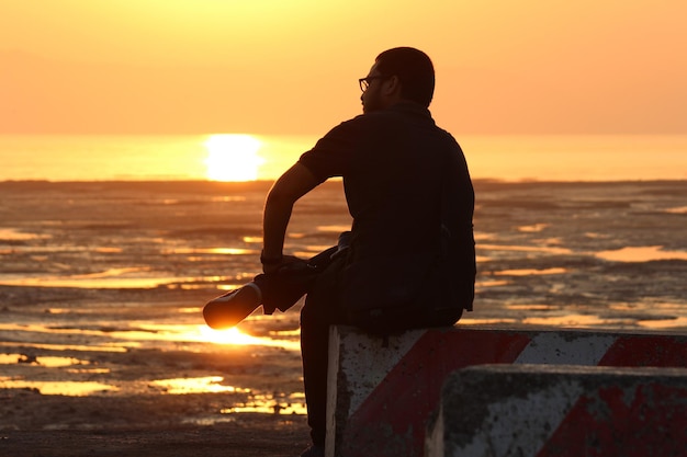 Silhouette d'un homme assis sur la plage au coucher du soleil
