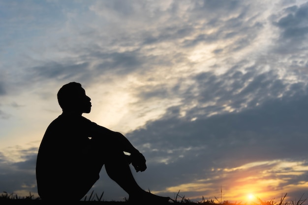 Silhouette d'un homme assis avec si triste au coucher du soleil.