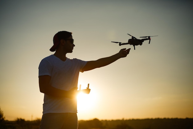 Silhouette d'un homme attrapant un drone avec une main et une télécommande dans une autre main au coucher du soleil