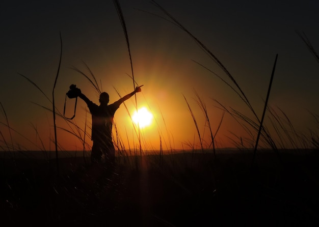 Photo silhouette d'un homme avec les bras tendus sur le champ contre le ciel au coucher du soleil