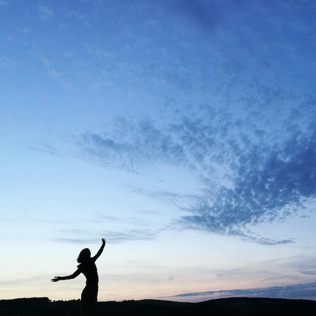 Photo silhouette d'un homme avec les bras tendus contre le ciel au coucher du soleil