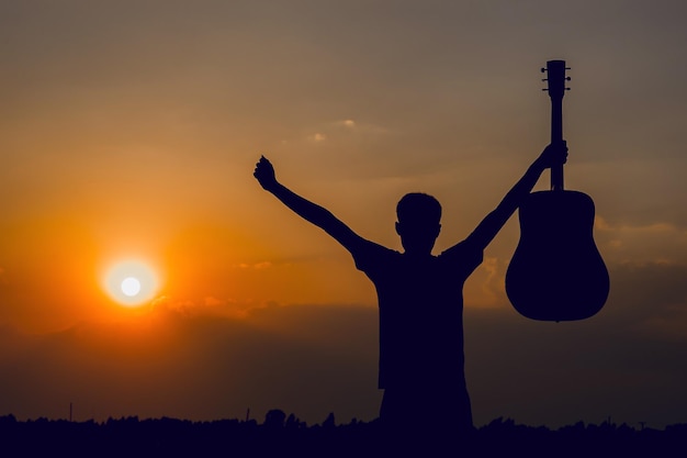 Silhouette d'un homme avec les bras tendus tenant une guitare au lever du soleil