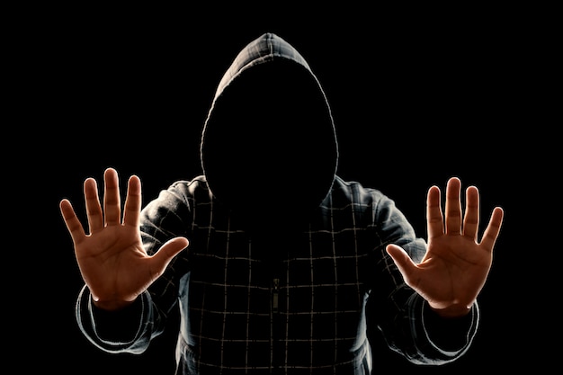Silhouette d'un homme en cagoule sur un fond noir, le visage n'est pas visible, montre les paumes de la caméra.