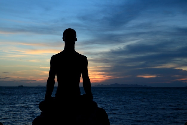 Silhouette de l'homme corps parfait agit yoga sur le rocher avec un espace de coucher de soleil sur la mer