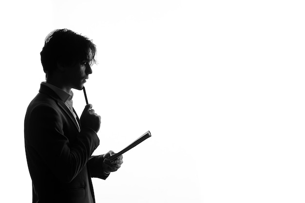 Photo silhouette d'homme en costume strict prenant des notes vue de côté ombre arrière-plan blanc éclairé