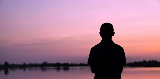 Silhouette d'homme debout au bord du lac contre le ciel au coucher du soleil