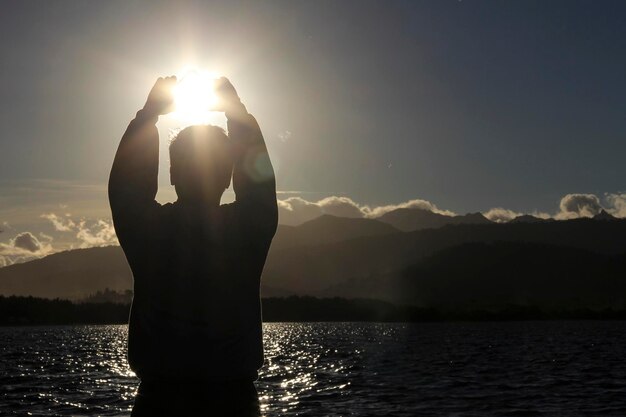 Silhouette d'un homme debout au bord d'un lac contre les montagnes au coucher du soleil