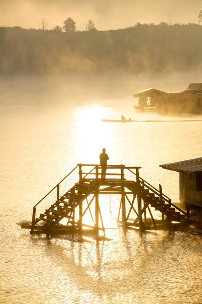 Photo silhouette d'un homme debout au-dessus de la mer au coucher du soleil