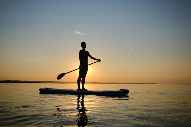 Photo silhouette d'un homme debout dans la mer contre le ciel au coucher du soleil