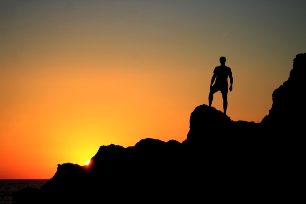 Silhouette d'un homme sur une falaise contre un ciel orange