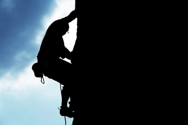 Photo silhouette d'homme grimpant sur un rocher sur fond de ciel bleu