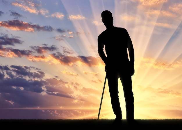 La silhouette d'un homme handicapé se soutient avec une béquille sur fond de coucher de soleil. Concept de personnes en réadaptation