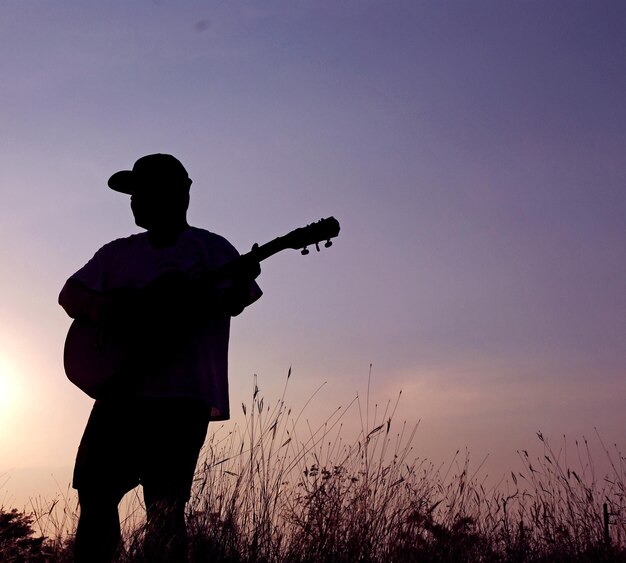 Silhouette d'un homme jouant de la guitare sur le terrain contre le ciel au coucher du soleil