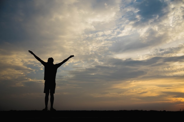 Silhouette d'un homme avec les mains levées au coucher du soleil.