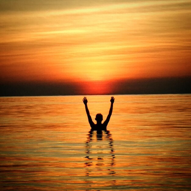 Silhouette d'un homme en mer contre le ciel au coucher du soleil