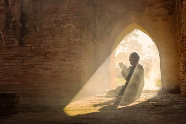 La silhouette d'un homme musulman asiatique, qui prie dans une pièce avec la lumière du soleil qui brille à travers la porte de la mosquée