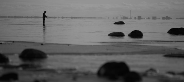 Photo silhouette d'un homme pêchant alors qu'il se tient en mer contre le ciel