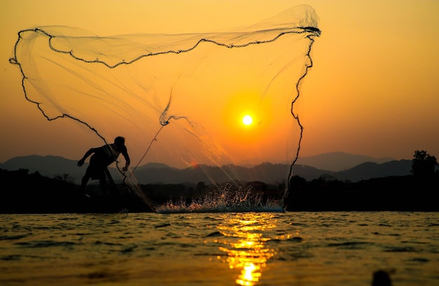 Silhouette d'un homme pêchant au lac contre le ciel au coucher du soleil