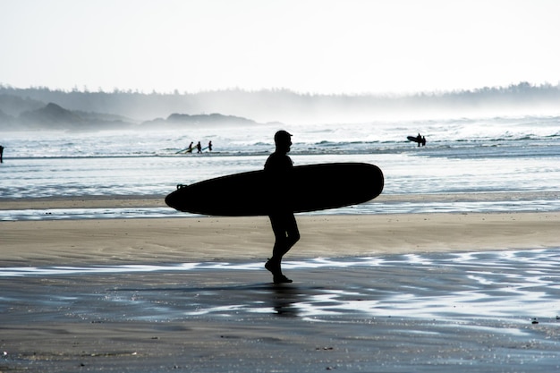 Silhouette d'un homme avec une planche de surf marchant sur la plage