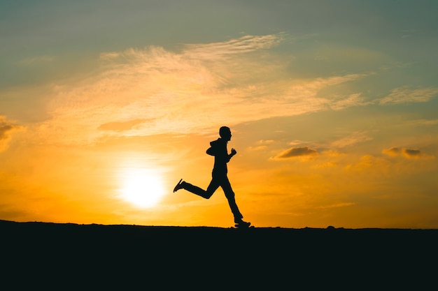 Silhouette d'un homme qui court sur une route rurale pendant le coucher du soleil