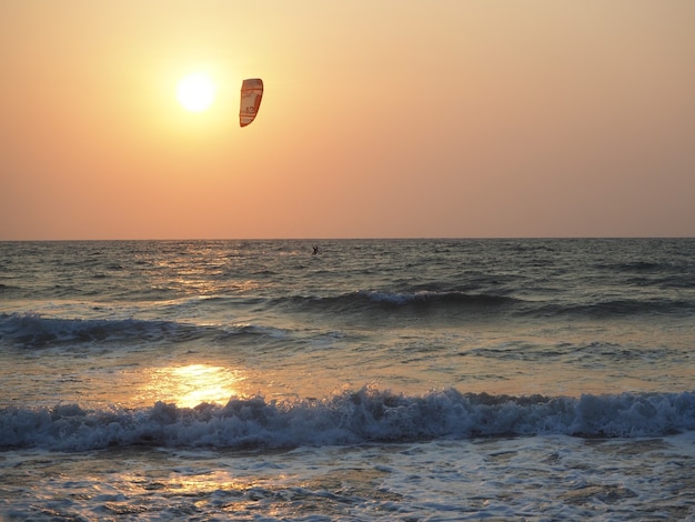 Silhouette d'un homme qui se promène dans la mer en kitesurf dans les rayons du soleil couchant. Sports nautiques extrêmes