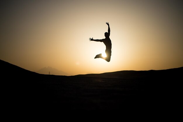 Silhouette d'homme sautant au ciel coucher de soleil