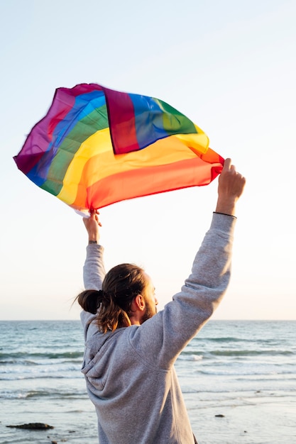 silhouette d'un homme tenant un drapeau arc-en-ciel de la fierté gaie dans le vent sur une plage tropicale avec un soleil doré