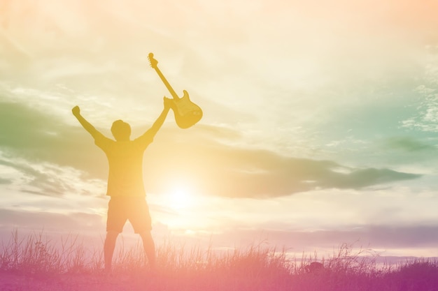 Silhouette d'un homme tenant une guitare alors qu'il se tient sur la terre contre le ciel au coucher du soleil