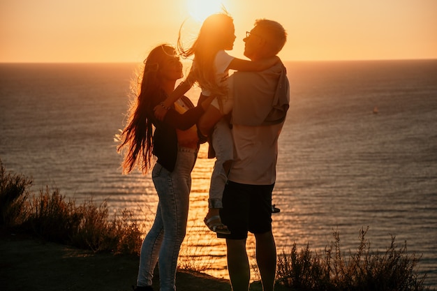 Silhouette d'un jeune couple romantique avec un enfant profitant de la soirée sur une falaise au-dessus de la mer