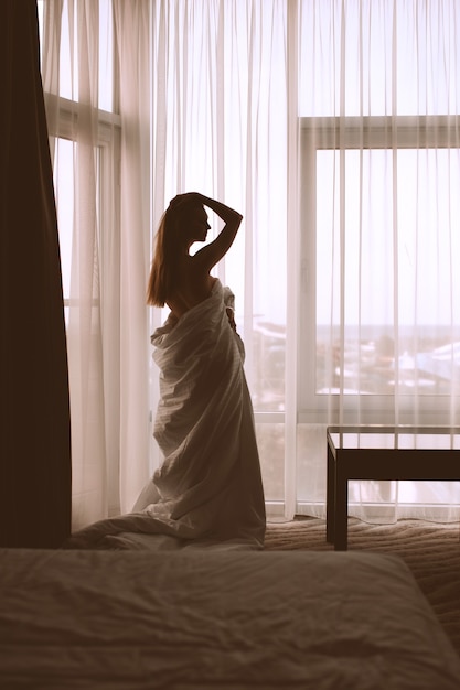 Silhouette de jeune femme debout au-dessus de la fenêtre dans la chambre d'hôtel