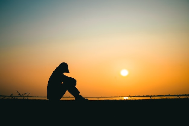 Silhouette d'une jeune femme debout regardant tristement le ciel au coucher du soleil