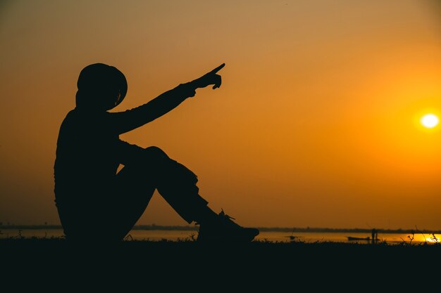 Silhouette d'une jeune femme debout regardant tristement le ciel au coucher du soleil