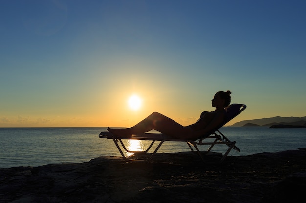 Silhouette de la jeune femme est allongée sur le transat au coucher du soleil