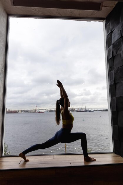 Silhouette de jeune femme faisant du yoga en pose de héros. Concept d'entraînements à domicile en quarantaine. Publicité