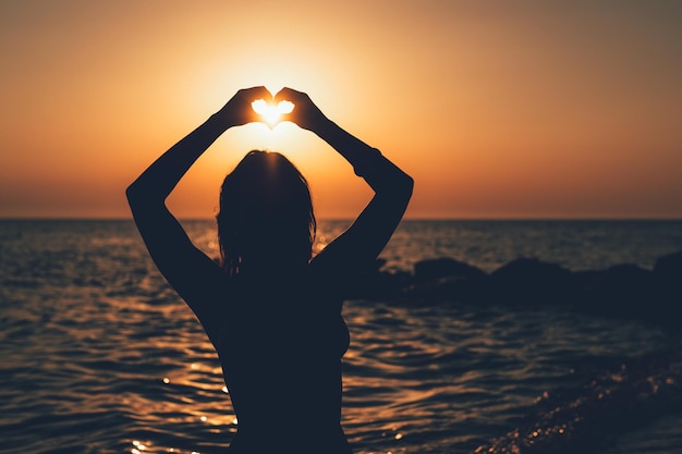 Silhouette de jeune femme heureuse appréciant au coucher du soleil sur la plage. Elle s'amuse et tient le soleil.