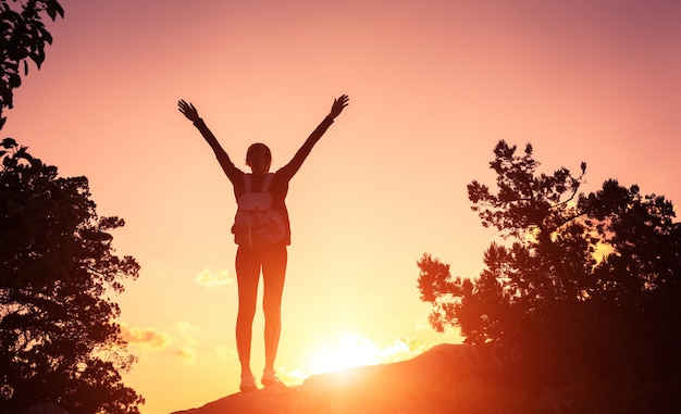 Silhouette d'une jeune femme heureuse dans les montagnes au coucher du soleil