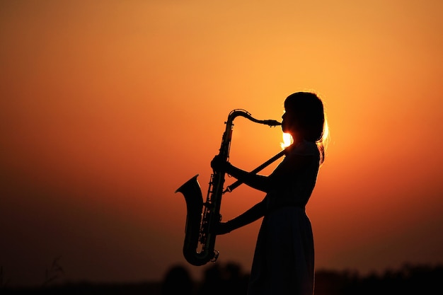 Silhouette jeune femme jouant du saxophone pendant le coucher du soleil, Thaïlande