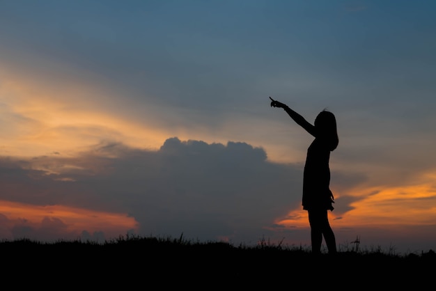 Silhouette jeune femme pointant vers l'avant pour rêver à venir dans le ciel coucher de soleil